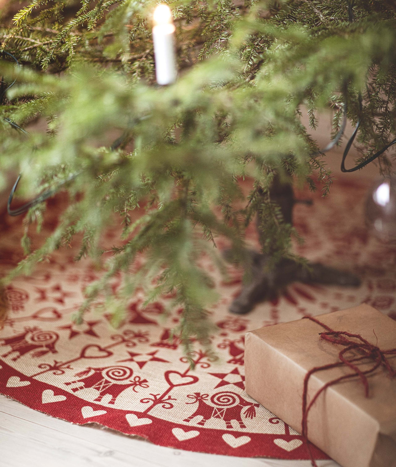 Julgransmatta Mammas jul tryckt på jute i röd färgställning placerad under julgran. Julmatta med hjärtan, julbockar, stjärnor, juläpplen och folkliga symboler